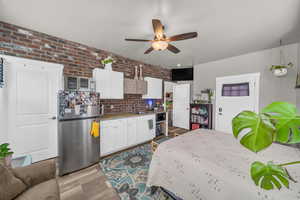 Kitchen featuring ceiling fan, light hardwood / wood-style floors, brick wall, stainless steel fridge, and sink