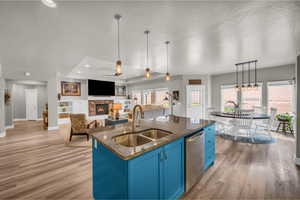 Kitchen featuring light wood-type flooring, stainless steel dishwasher, an island with sink, blue cabinets, and sink