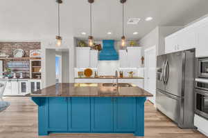 Kitchen with appliances with stainless steel finishes, sink, pendant lighting, premium range hood, and light wood-type flooring