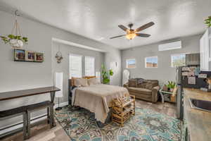 Bedroom featuring a wall mounted air conditioner, light wood-type flooring, ceiling fan, and stainless steel fridge