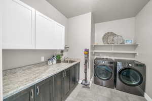 Laundry area with sink, cabinets, washing machine and dryer, and light tile patterned flooring