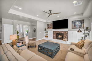 Living room featuring a fireplace, a tray ceiling, light hardwood / wood-style floors, and ceiling fan