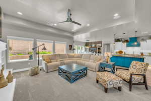 Carpeted living room with plenty of natural light, sink, ceiling fan, and a raised ceiling