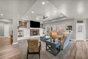 Living room with ceiling fan, a tray ceiling, light hardwood / wood-style flooring, and a brick fireplace