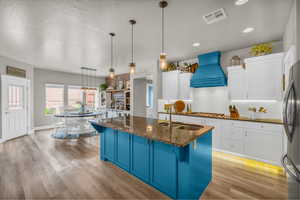 Kitchen with decorative light fixtures, custom exhaust hood, sink, light hardwood / wood-style flooring, and backsplash