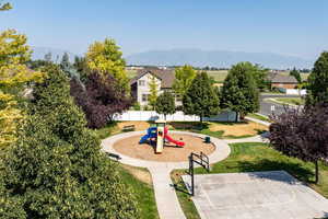 View of home's community with a mountain view, basketball court, a playground, and a lawn