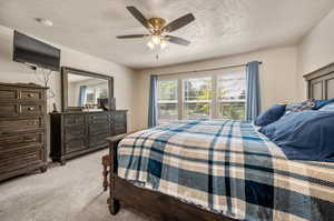 Bedroom with light colored carpet, a textured ceiling, and ceiling fan