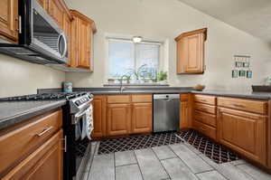 Kitchen with sink, appliances with stainless steel finishes, light tile patterned floors, and vaulted ceiling