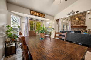 Dining room with a stone fireplace, a wealth of natural light, lofted ceiling, and ceiling fan