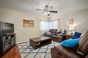 Living room with a textured ceiling, wood-type flooring, and ceiling fan