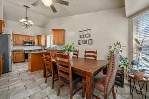 Dining area with ceiling fan with notable chandelier, light tile patterned floors, and vaulted ceiling