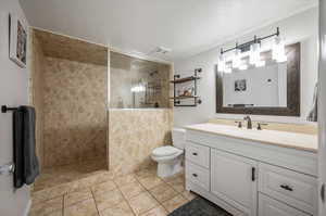 Bathroom featuring vanity, tile patterned floors, tile walls, a tile shower, and toilet