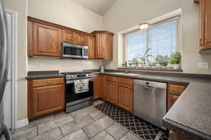 Kitchen with light tile patterned floors, vaulted ceiling, appliances with stainless steel finishes, and sink