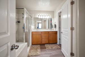 Bathroom with a shower with door, a textured ceiling, dual bowl vanity, and hardwood / wood-style floors