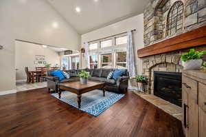 Living room with a stone fireplace, wood-type flooring, and high vaulted ceiling