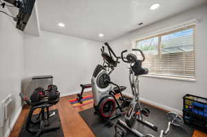 Workout room with light wood-type flooring and a textured ceiling