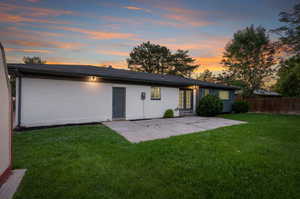 Back house at dusk featuring a patio area and a lawn