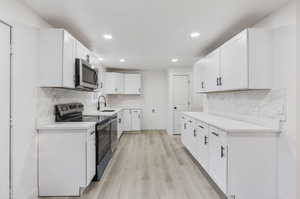 Kitchen with white cabinetry, stainless steel appliances, light hardwood / wood-style floors, and tasteful backsplash