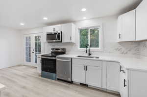 Kitchen featuring white cabinetry, light hardwood / wood-style flooring, backsplash, stainless steel appliances, and sink