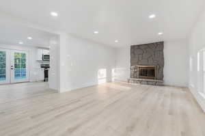 Unfurnished living room featuring light hardwood / wood-style flooring, a stone fireplace, and french doors