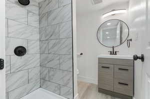 Bathroom with tiled shower, toilet, hardwood / wood-style floors, and vanity