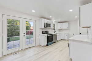 Kitchen with light hardwood / wood-style flooring, french doors, white cabinets, backsplash, and stainless steel appliances