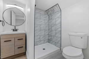 Bathroom with vanity, toilet, a tile shower, and wood-type flooring