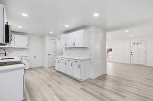 Kitchen with light hardwood / wood-style flooring, white cabinets, and backsplash