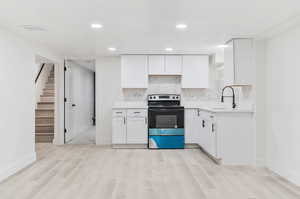 Kitchen with white cabinets, sink, range with electric cooktop, and light wood-type flooring