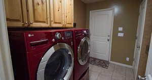 Washroom featuring light tile patterned floors, washer and clothes dryer, and cabinets