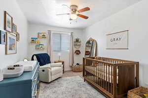 Carpeted bedroom featuring a crib and ceiling fan