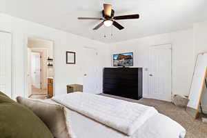 Bedroom featuring two closets, connected bathroom, carpet floors, and ceiling fan