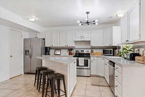 Kitchen with white cabinetry, light tile patterned floors, a kitchen island, stainless steel appliances, and decorative backsplash