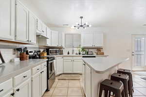 Kitchen featuring light tile patterned flooring, backsplash, appliances with stainless steel finishes, and white cabinets