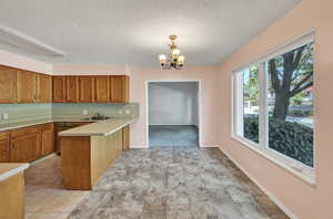 Kitchen with light tile patterned floors, a chandelier, pendant lighting, a textured ceiling, and kitchen peninsula