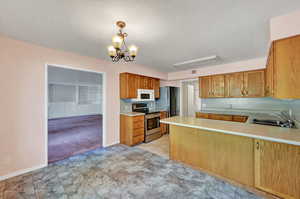 Kitchen with a notable chandelier, kitchen peninsula, appliances with stainless steel finishes, light carpet, and sink