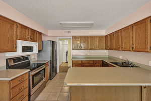 Kitchen with stainless steel appliances, sink, kitchen peninsula, a textured ceiling, and light tile patterned flooring