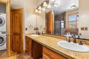 Bathroom featuring stacked washer / drying machine, tile patterned flooring, and dual bowl vanity