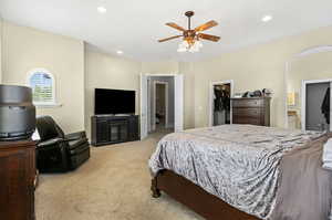 Bedroom with ensuite bathroom, a closet, light colored carpet, a walk in closet, and ceiling fan