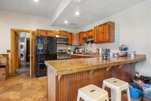 Kitchen featuring light tile patterned flooring, kitchen peninsula, stacked washer / drying machine, stainless steel appliances, and a kitchen bar