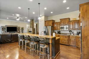 Kitchen featuring ceiling fan, stainless steel appliances, a kitchen bar, dark hardwood / wood-style floors, and a spacious island