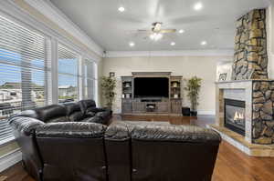 Living room with a stone fireplace, crown molding, hardwood / wood-style floors, and ceiling fan