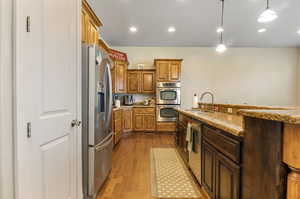 Kitchen with appliances with stainless steel finishes, sink, pendant lighting, light stone counters, and light wood-type flooring