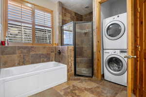 Laundry room featuring stacked washer and dryer, tile patterned floors, and a healthy amount of sunlight