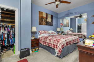 Carpeted bedroom with a textured ceiling, ceiling fan, and a closet