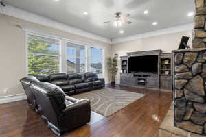 Living room with ornamental molding, ceiling fan, and dark wood-type flooring