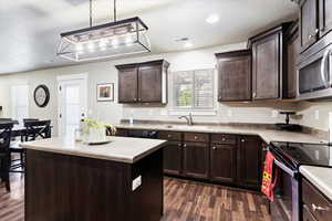 Kitchen featuring appliances with stainless steel finishes, sink, hanging light fixtures, a center island, and dark wood-type flooring