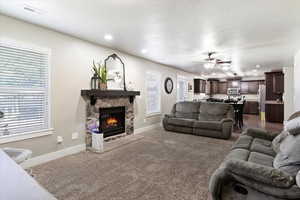 Living room with a stone fireplace, carpet flooring, a textured ceiling, and ceiling fan