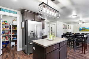 Kitchen with dark brown cabinets, dark hardwood / wood-style flooring, a kitchen island, ceiling fan, and stainless steel fridge