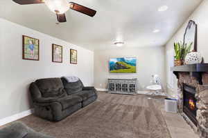 Carpeted living room with a stone fireplace and ceiling fan